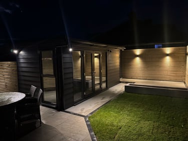 Modern garden room at night with outdoor lighting, patio, and lawn, creating an inviting backyard oasis.