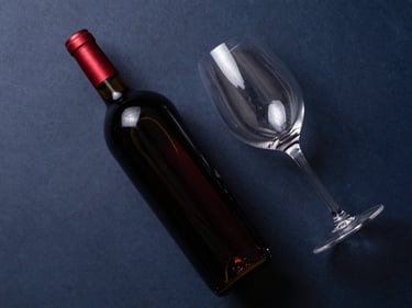 Overhead flat-lay of a dark red wine bottle and a wine glass, soft natural light, minimalist setting.