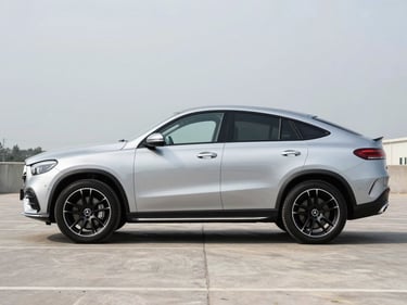 Side-profile shot of a silver Mercedes-Benz GLE Coupe parked on a clean concrete forecourt, overcast daylight, no people, wheel arch and side mirror detail sharp