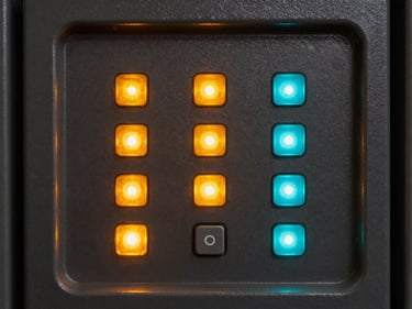 Close-up of an alarm control panel with illuminated status LEDs in amber and cyan, keypad buttons in sharp focus, dark metal housing with rim lighting revealing form detail