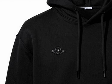 Tight macro product detail of a black custom-embroidered hoodie, high-key studio lighting, sharp dramatic shadows, black and white tones, 50mm lens
