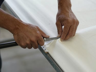 Close-up overhead shot of a technician's hands grinding a fiberglass hull joint, fresh laminate visible, workshop floor below, north-facing daylight, no faces