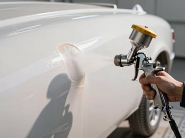 Close-up of a spray gun applying gelcoat to a hull surface, fine mist catching north-facing daylight, freshly painted white surface beside masked bare area, no faces visible
