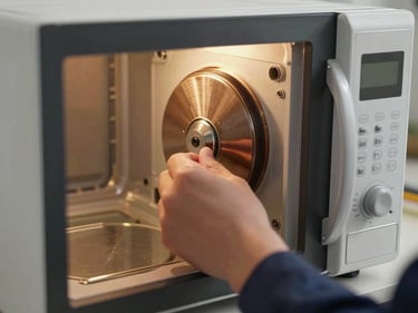 Close-up of a technician's hand opening a microwave door to inspect the interior magnetron area, warm kitchen tungsten light, tight on the cavity and hand