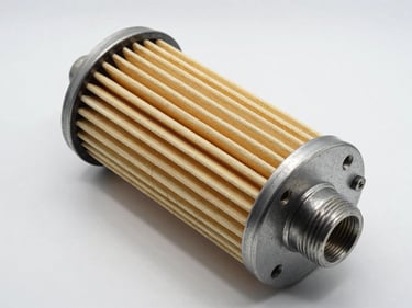 Studio strobe flat-lay of an industrial oil separator filter cartridge on a white surface — spiral-wound glass fibre element, metal end caps, threaded port visible, high contrast lighting showing surface texture and exact dimensions