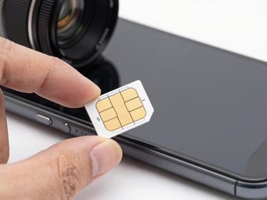 Macro close-up of a nano-SIM card being held between two fingers over a phone tray, bright daylight studio lighting, white background, sharp technical focus