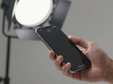 Close-up of a hand holding a smartphone with a network signal strength screen visible, bright studio overhead lighting, neutral background, clean technical composition