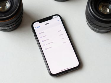 Overhead flat-lay of a smartphone displaying network APN settings menu on a clean white desk, bright even studio lighting, precise technical framing