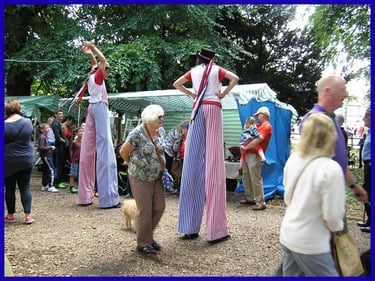 Performers on stilts in red white and blue striped costumes entertain crowds at an outdoor festival.