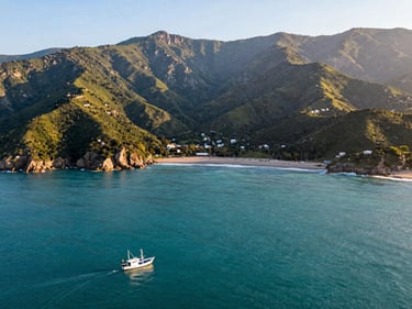 Wide shot of Santa Marta bay from above, turquoise water meeting green Sierra Nevada foothills, a small fishing boat in the foreground, warm morning light