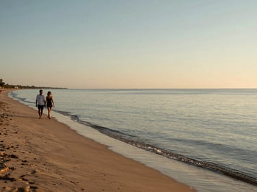 Coveñas beach at late afternoon, calm shallow water, a couple walking along the shoreline to the left, wide open sky, warm amber light on the sand