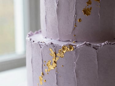 An elegant bespoke birthday cake with modern textured frosting and gold leaf accents, close-up shot.