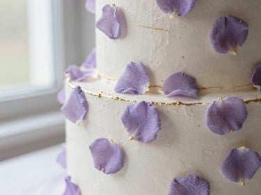 A luxury anniversary cake decorated with soft lavender sugar petals and delicate gold lines, romantic lighting.