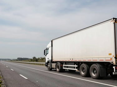 Environmental wide shot of a large moving truck on an open highway at midday, overcast sky, empty road stretching ahead, truck occupying the right third of the frame