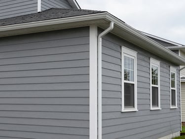 Wide environmental shot of a residential exterior facade, freshly painted gray siding with white trim detail, overcast daylight, no people, clean gutters and downspouts visible