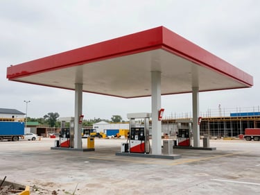 Wide environmental photo of a fuel station canopy and pump island framework under active construction, steel support columns visible, overcast daylight, site equipment in background showing project scale