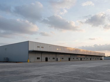 Wide-angle perspective of a massive logistics warehouse under construction, dramatic overcast sky, cool morning light