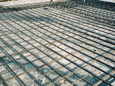 Low-angle shot of concrete pouring on steel reinforcement grid, sharp morning daylight, cool steel and slate tones