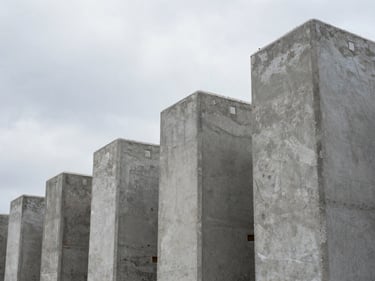 Close-up overhead shot of stacked precast concrete columns on a construction yard, grade markings visible on the faces, overcast natural daylight, no people