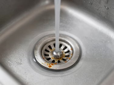 Close-up of a kitchen sink drain completely blocked with residue, standing grey water visible, practical work-light from above, realistic documentary framing