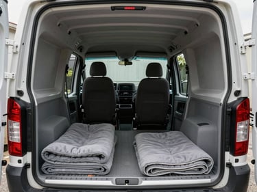 Interior of a compact cargo van, natural daylight entering from rear doors, padded blankets folded on the floor, clean empty load area showing modest volume, close perspective from driver-side loading edge