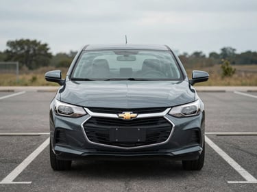 Front view of a dark gray Chevrolet Onix sedan parked straight-on in a daylight parking lot, overcast lighting, clean asphalt