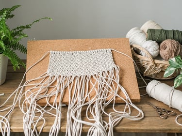 Proyecto de tapiz de macramé hecho a mano en proceso sobre un tablero de corcho.