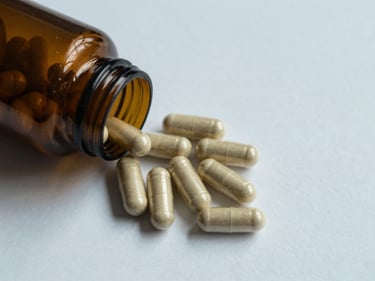 Overhead flat-lay of magnesium glycinate capsules spilled from an open amber bottle onto a white surface, cool north-facing daylight, clinical isolation framing