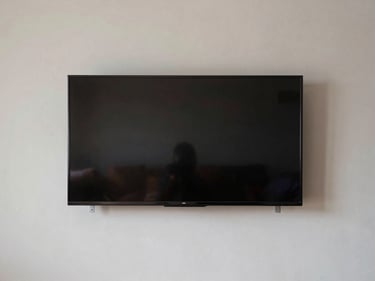 Wide shot of a flat-screen TV flush-mounted on a painted drywall, level and centered, mounting bracket hardware visible at edges, daylight-neutral interior, no people