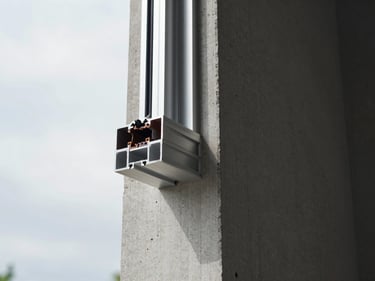 Close-up of an aluminum window frame corner joint on a building exterior, overcast daylight, precise miter seal visible, raw concrete wall surround, installation in progress