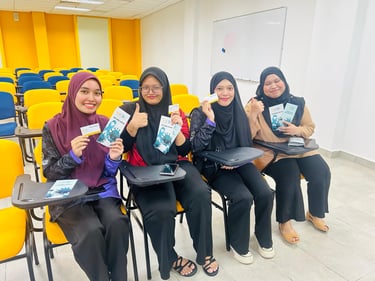 Four smiling female students in hijabs hold health awareness brochures in a university classroom.