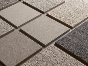 Overhead flat-lay of contemporary broadloom carpet tile samples arranged in a grid — neutral warm grey and charcoal cut-pile modules, soft studio daylight emphasising pile texture and edge precision
