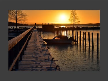 a boat is docked at the end of a pier at a winter sunset