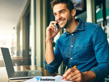 a man sitting at a table with a laptop and a notebook and making a phone call