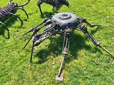 A metal spider sculpture made from recycled car parts and scrap metal on a green lawn.