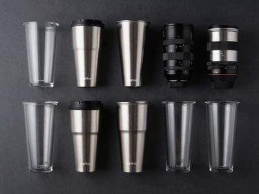 Overhead studio flatlay of Starline branded drinkware assortment on a dark matte surface, even cold studio lighting, silver and black product finishes, clean shadows, no text visible