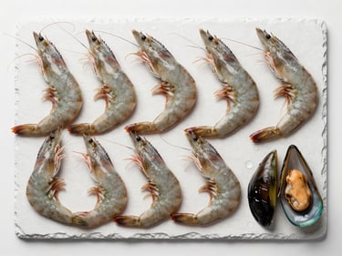 Overhead flat-lay of fresh whole shrimp and mussels arranged on white slate under cool diffused studio light, water droplets visible, clean and precise, no warm tones