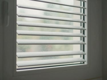 Environmental photograph of a UPVC louvre window with angled glass blades in an Indian bathroom wall, diffused natural light filtering through the angled slats, white UPVC frame intact