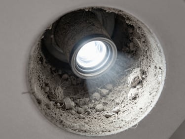 Close-up macro shot of residential AC duct interior, thick grey dust coating every surface under bright flashlight, fibres and debris visible in sharp detail, overhead angle inside the duct