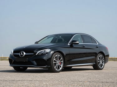 2018 Mercedes-Benz C-Class black sedan photographed three-quarter front profile on tarmac, bright studio daylight, no people, full vehicle in frame