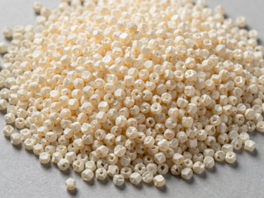 Macro overhead shot of polypropylene resin pellets in natural off-white and cream, poured onto a flat industrial surface, studio strobe lighting highlighting pellet uniformity and size consistency