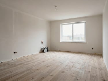 Freshly finished room interior after restoration turnover, new drywall painted, clean flooring installed, daylight through bare window, no furniture, construction tools staged neatly against the far wall