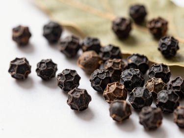Macro shot of whole black peppercorns and dried bay leaves on a clean surface, soft warm natural light.