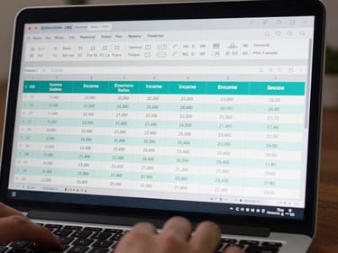 Close-up of a laptop screen displaying a bookkeeping ledger interface with income and expense rows, teal accent highlights on key figures, dark UI theme, hands on keyboard visible at bottom edge