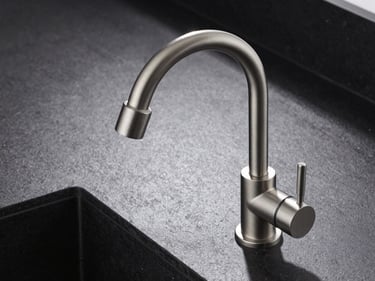 Overhead tight shot of a brushed-nickel kitchen mixer tap mounted on a dark stone countertop, architectural documentation lighting, sharp shadows defining the high-arc spout form, no hands, no food, no lifestyle context
