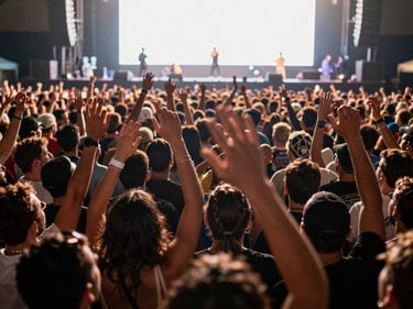 Close-up overhead of a sold-out reggaeton concert floor, crowd hands raised, stage glow from front, natural venue atmosphere