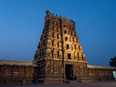 Wide shot of a Tamil Nadu temple gopuram at dusk, dramatic layered stone carvings catching last light against a deep blue sky, empty forecourt in the foreground, no tourists