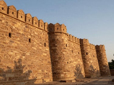 Close study of Jaisalmer sandstone ramparts at dawn, warm amber light raking across carved battlements, deep shadow in the crevices, no people, wide environmental framing