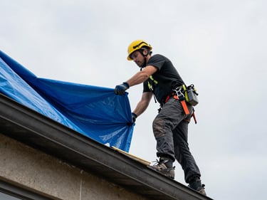 Action shot from below looking up at roofers stretching a blue emergency tarp across a storm-damaged Sioux City roofline, overcast sky behind, tarp edges being secured at the ridge