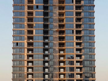 Straight-on facade detail of a Creek Harbour off-plan tower under construction, scaffolding removed from lower floors revealing glass skin, golden-hour light, wide environmental frame